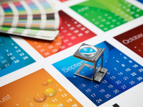 A printers eye glass sitting on a colourful calendar